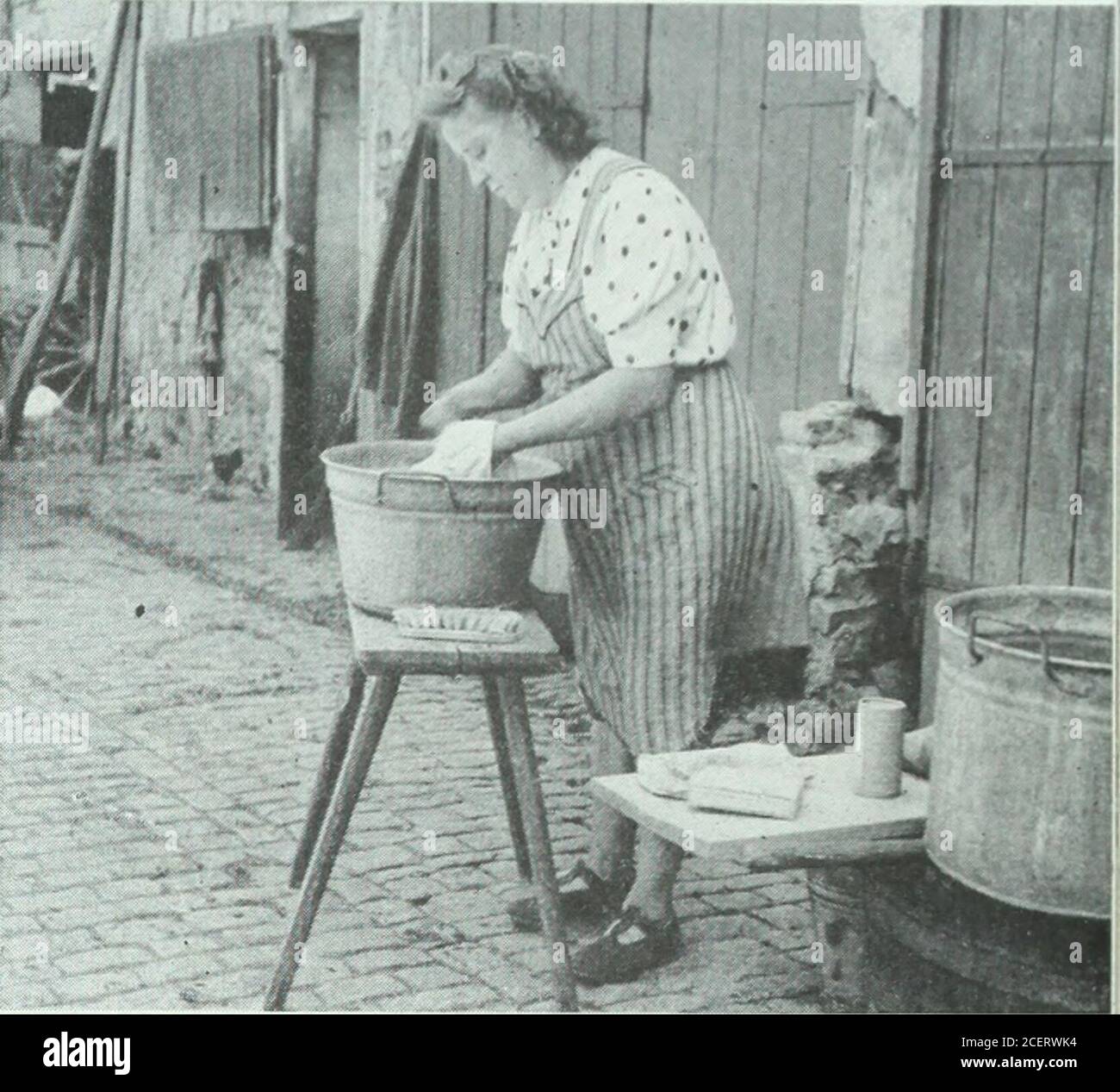 . Le journal de la maison des dames. PHOTOGRAPHIES pour le Journal par Horace Brijtol (Japon et Chine), Larry Burrows (Angleterre), Robert CAPA (États-Unis et Tchécoslovaquie), Marie Hansen (Italie), George Rodger (Égypte, Pakistan et Afrique équatoriale), Phil Schultz (Mexique), David Seymour (France et Allemagne). ALLEMAGNE: Une fois par mois Frau Stieglitz. Fait une grande buanderie avec l'aide d'une femme qui vit dans son village de Wollau, près du Rhin.ici elle fait son petit lavage quotidien dans la cour pavée de la ferme. Le petit récipient en boîte contient de la poudre de savon précieuse. Banque D'Images