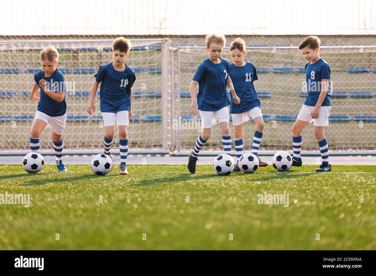 Groupe de garçons Kicking Soccer balles sur terrain de sport de gazon. Équipe de sports pour enfants sur l'entraînement de football scolaire. Happy Kids Making Sports Banque D'Images
