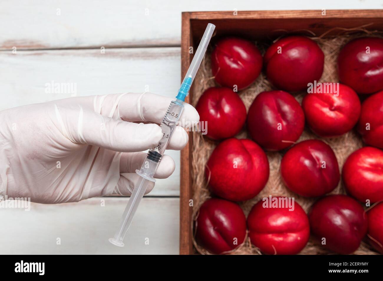 Main dans des gants médicaux tenant une seringue avec injection. En arrière-plan est une boîte en bois avec des nectarines. Le concept des aliments GM, légumes et fr Banque D'Images