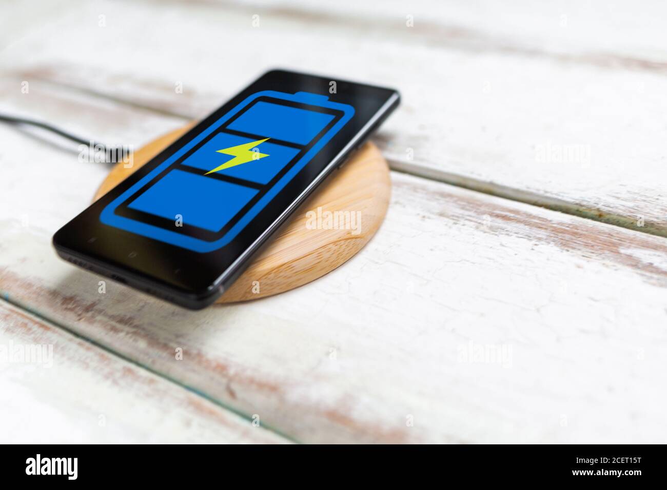 Concept des technologies modernes. Sur le chargeur sans fil se trouve un smartphone noir avec une icône de batterie bleue. Arrière-plan en bois blanc avec rayures diagonales. Banque D'Images