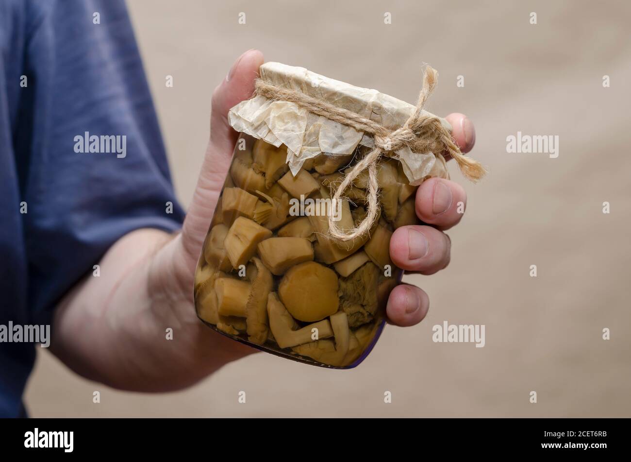 Les mains des hommes tiennent un pot en verre avec des champignons en conserve. Un bol transparent avec des morceaux de délicieux aliments. Aliments en conserve. Mise au point sélective. Banque D'Images