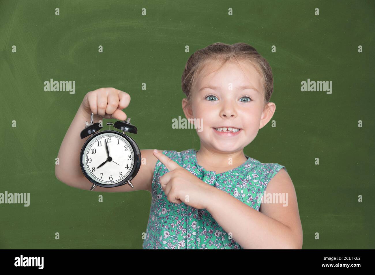 Une petite fille tient un réveil contre la commission scolaire verte. 8 heures, il est temps pour l'école. Photo de haute qualité Banque D'Images