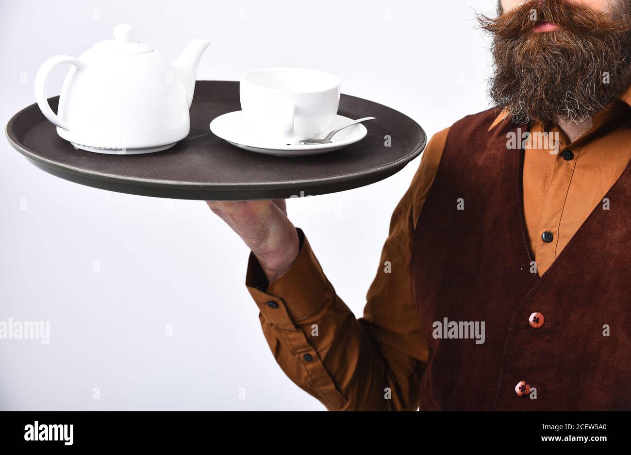 Le Barman en uniforme sert du café ou du thé. Concept de restauration de  restaurant. Un homme avec une barbe et une moustache tient le thé ou le  café sur fond blanc.