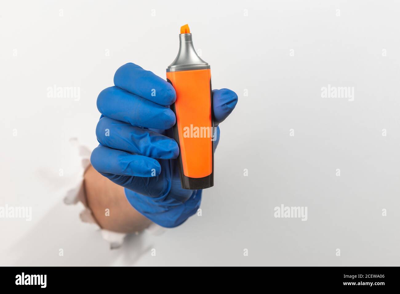 Main dans un gant en latex tenant un stylo surligneur orange à travers un  mur blanc déchiré Photo Stock - Alamy