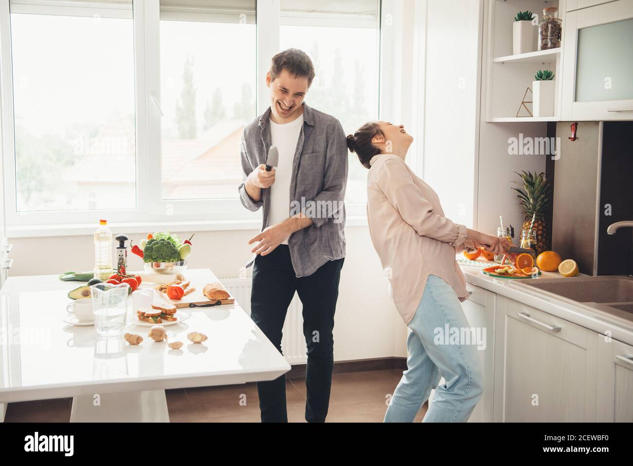 Couple caucasien cuisant dans la cuisine ensemble et sourire jouant et trancher des fruits Banque D'Images