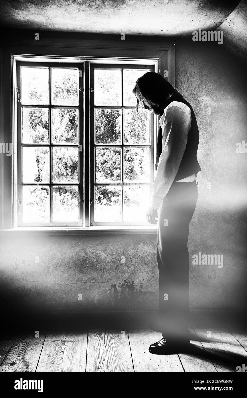 Image texturée en noir et blanc créative d'un triste homme devant une fenêtre. Banque D'Images