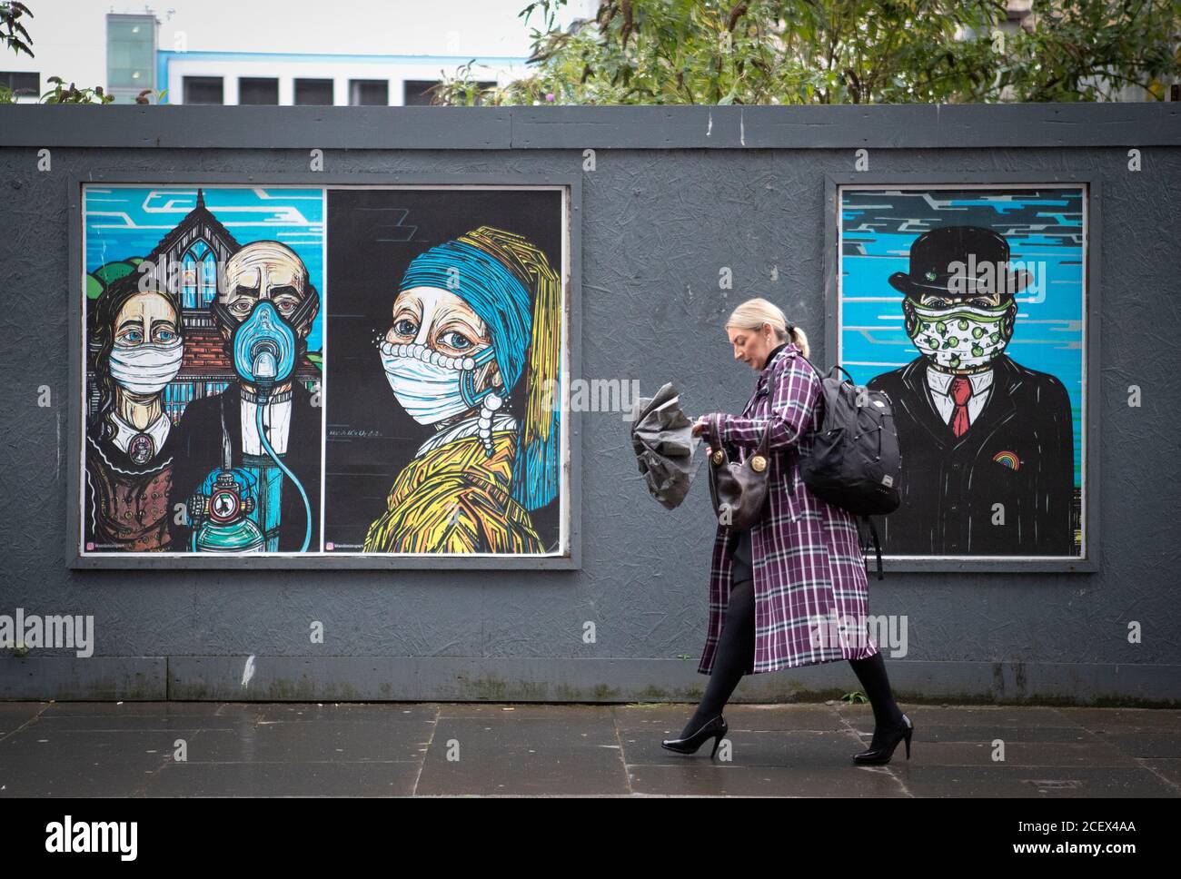 Une femme passe devant des affiches d'art de rue sur le thème du coronavirus dans le centre-ville de Glasgow. Banque D'Images