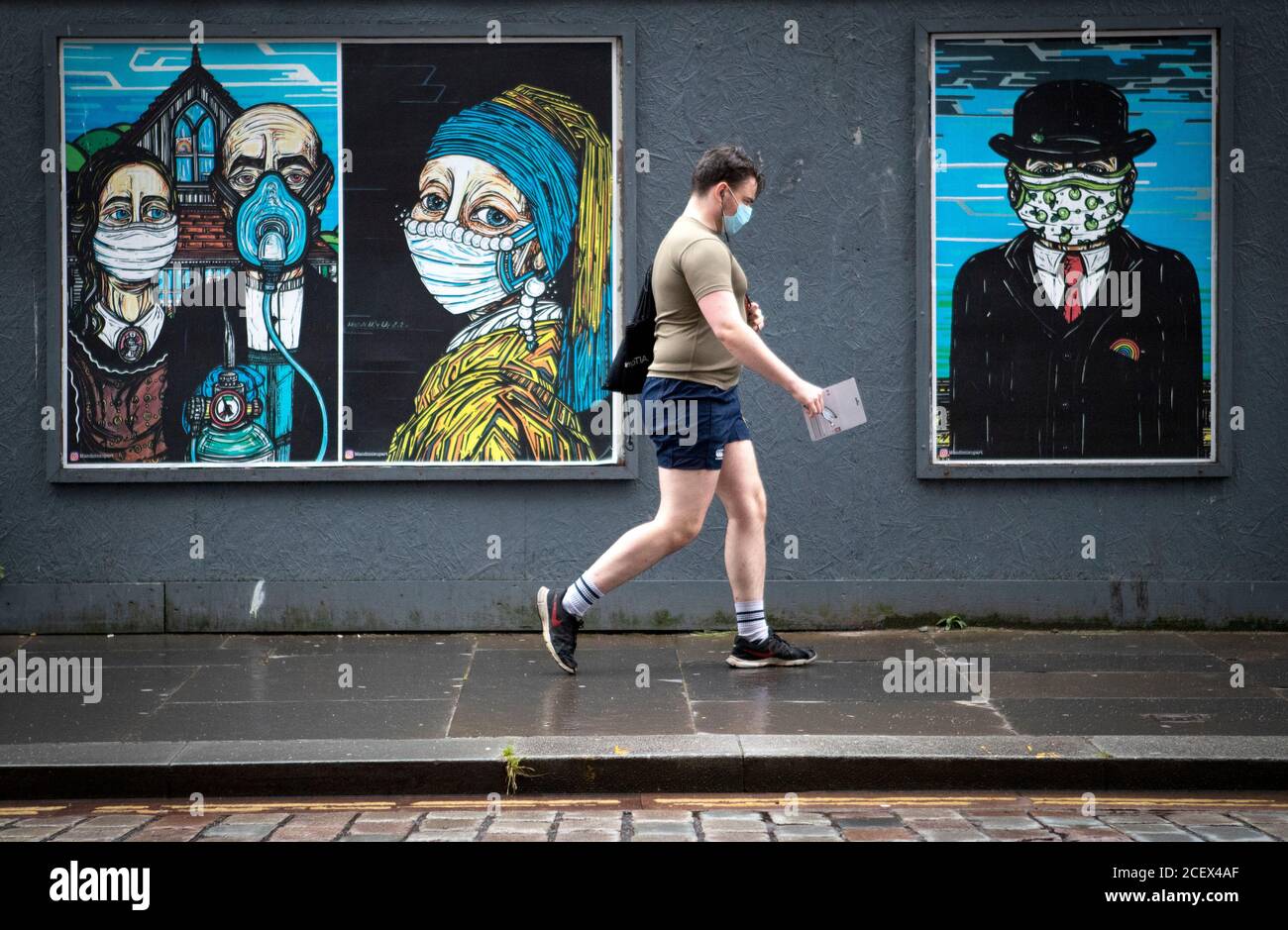 Un homme passe devant des affiches d'art de rue sur le thème du coronavirus dans le centre-ville de Glasgow. Banque D'Images