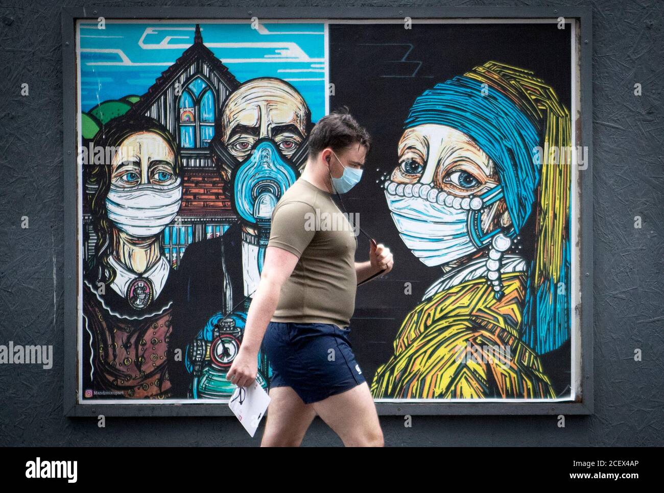 Un homme passe devant des affiches d'art de rue sur le thème du coronavirus dans le centre-ville de Glasgow. Banque D'Images