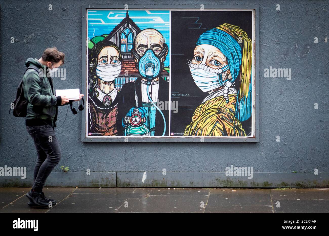 Un homme passe devant des affiches d'art de rue sur le thème du coronavirus dans le centre-ville de Glasgow. Banque D'Images