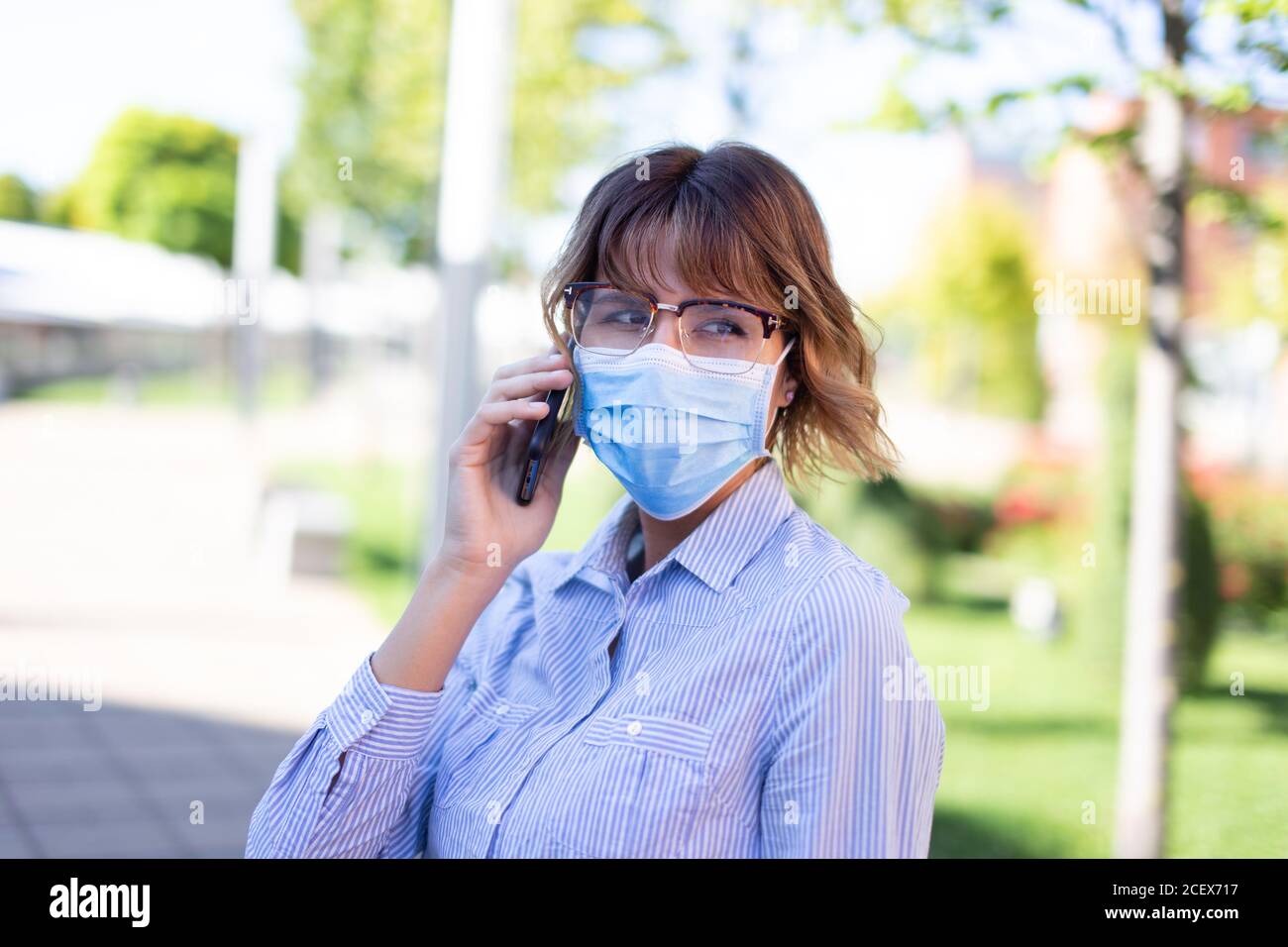 Jeune femme d'affaires dans le masque et les lunettes de vue appelant dans le parc à l'extérieur portrait à l'écart Banque D'Images