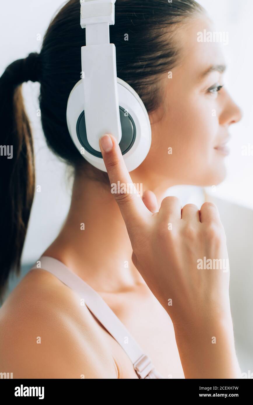 Mise au point sélective d'une jeune femme brunette touchant un casque pendant l'écoute musique à la maison Banque D'Images