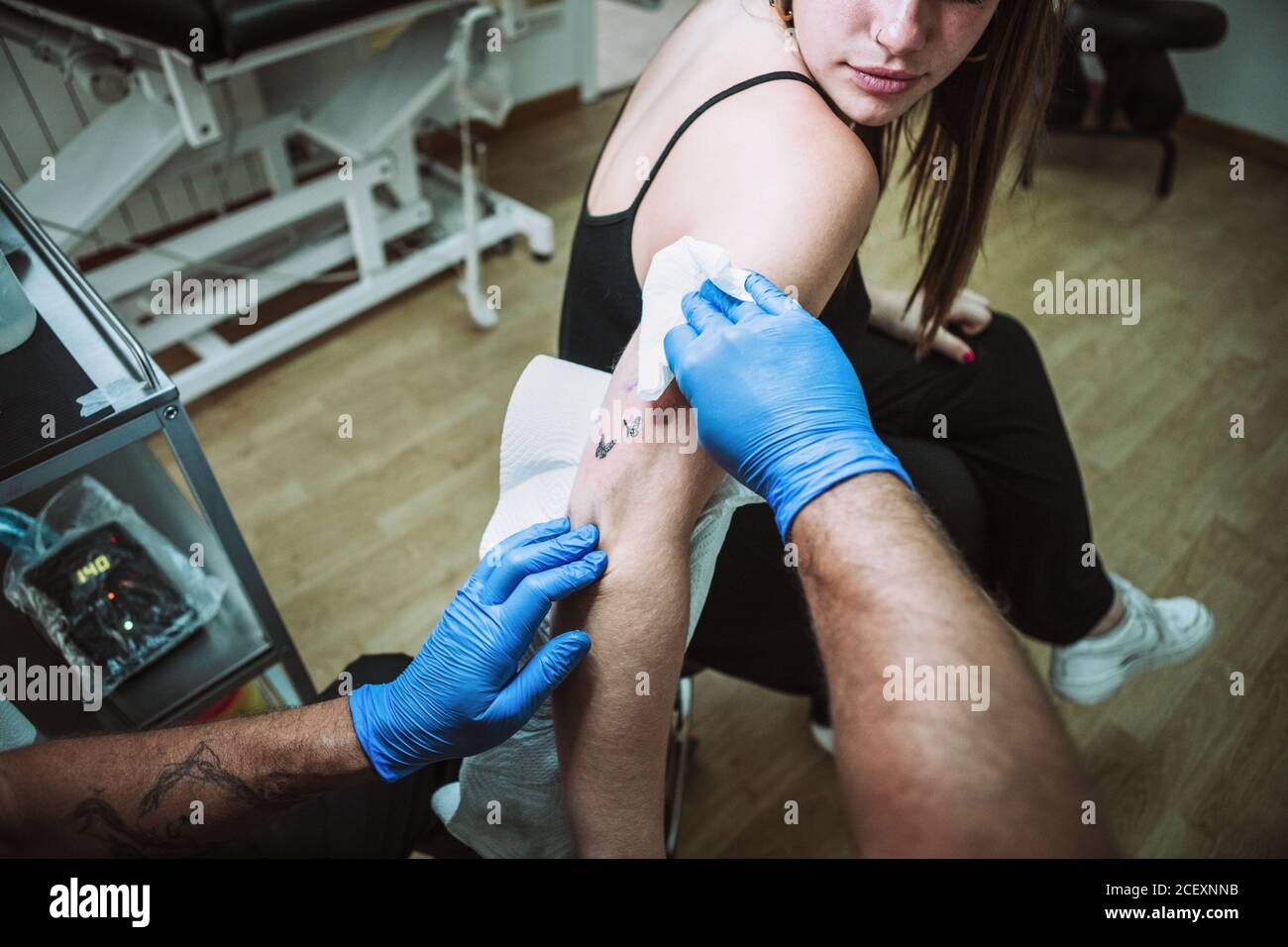 Vue arrière crop anonyme homme tatoueur en latex gants essuyant tatouage fraîchement préparé sur le bras de la cliente avec serviette en salon de coiffure Banque D'Images Vue arrière crop anonyme homme tatoueur en latex gants essuyant tatouage fraîchement préparé sur le bras de la cliente avec serviette en salon de coiffure Banque D'Images
