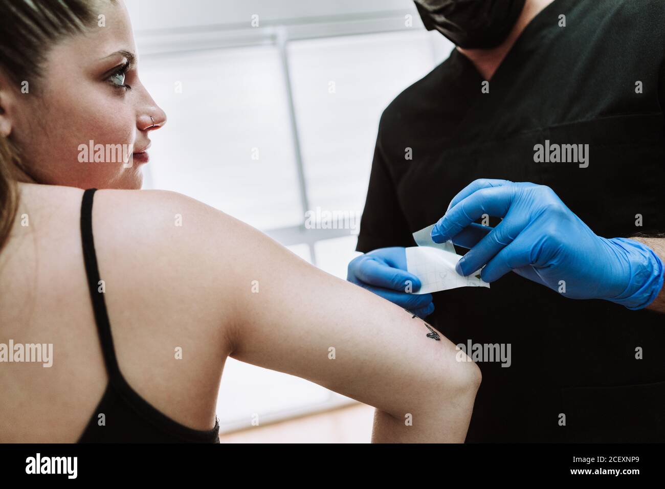 Crop anonyme homme tatoueur dans des gants de latex essuyant fraîchement fait tatouage sur le bras de la cliente femelle avec serviette de table pendant le travail en salon Banque D'Images Crop anonyme homme tatoueur dans des gants de latex essuyant fraîchement fait tatouage sur le bras de la cliente femelle avec serviette de table pendant le travail en salon Banque D'Images