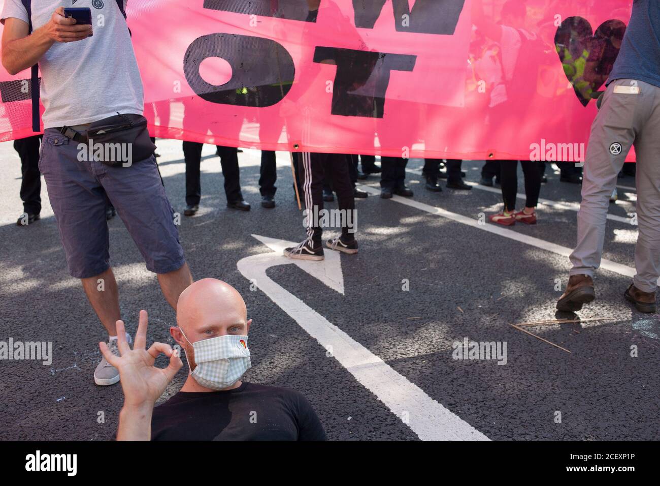 Un manifestant de la rébellion d'extinction se trouve sur la route, faisant le geste de la main OK devant une ligne de police lors des manifestations de 2020 à l'extérieur du Parlement. Banque D'Images