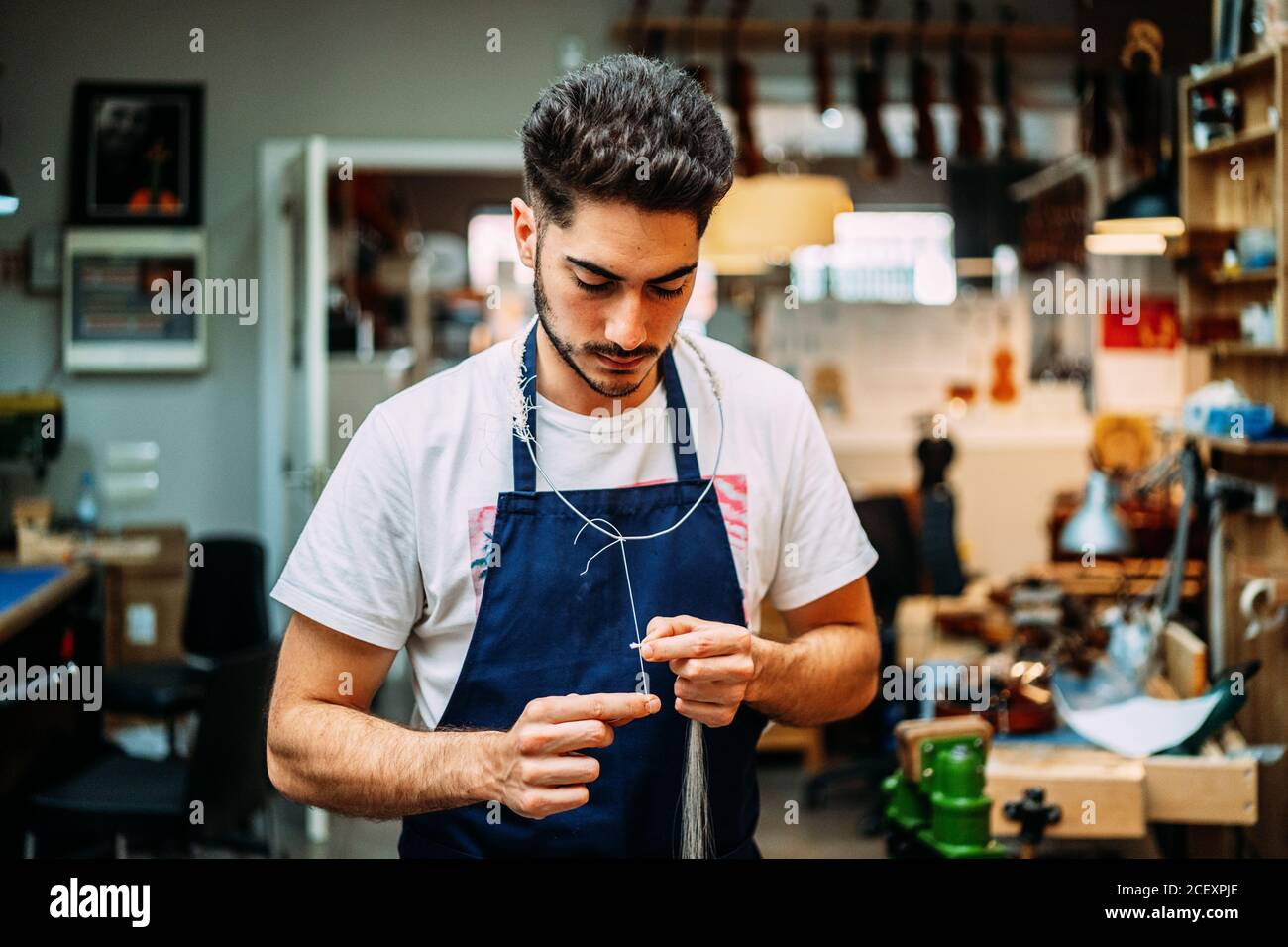 Jeune luthier spécialisé focalisé préparant le crin de cheval pour l'arc de violon pendant travaux de restauration dans un atelier moderne Banque D'Images