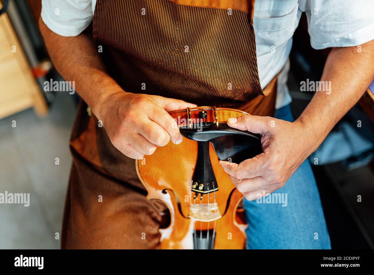Haut angle de récolte artisan anonyme tenant violon avec pince fixé sur la partie inférieure de l'instrument pendant les travaux de restauration Banque D'Images