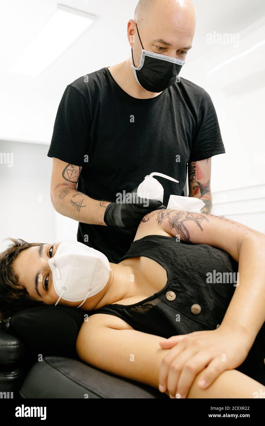 Tatoueur de sexe masculin dans un masque médical traitant le tatouage sur  le bras de femme avec un liquide spécial dans un salon contemporain Photo  Stock - Alamy