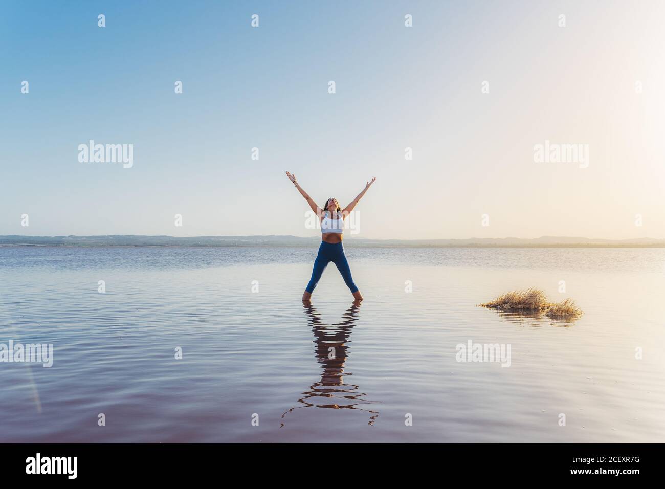 Corps complet d'une femme mince et méconnaissable en forme d'activewear debout Cinq étoiles pointues posent avec les bras vers le haut dans l'eau du lac en pratiquant le yoga en soirée d'été Banque D'Images