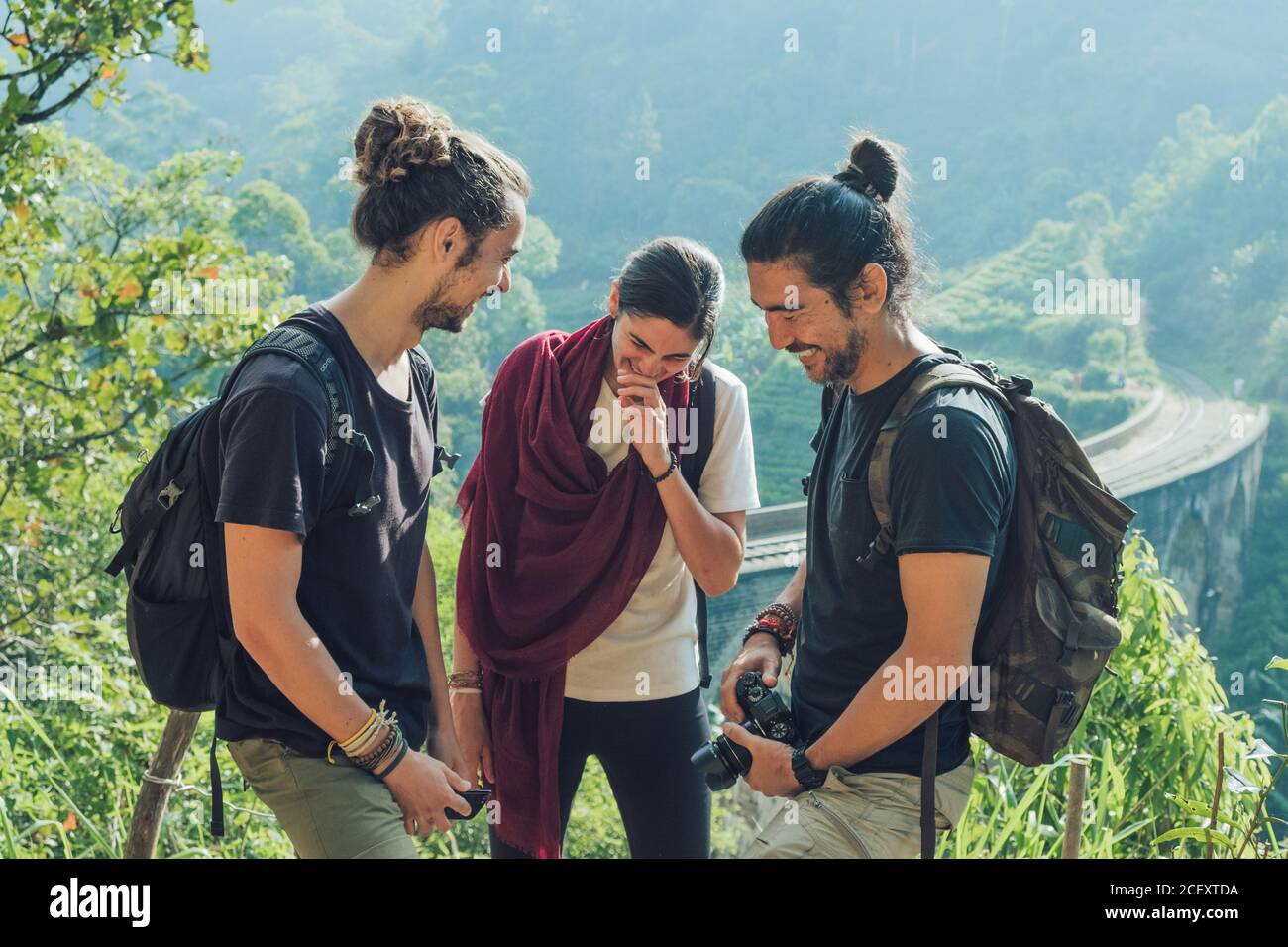 Groupe de jeunes amis multiethniques joyeux avec sacs à dos et photo appareil photo s'amusant et riant sur une colline verdoyante Près du vieux pont viaduc pendant les vacances d'été au Sri Lanka Banque D'Images