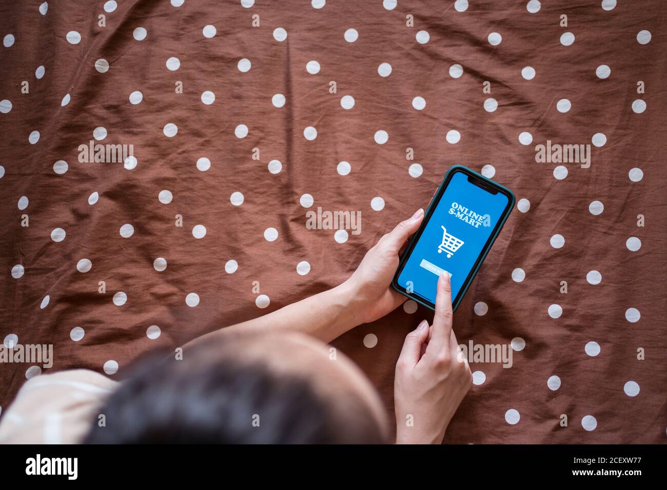 Du dessus de la récolte anonyme femelle couché sur le lit et utilisation de l'application en ligne sur le téléphone portable pour commander des aliments Banque D'Images