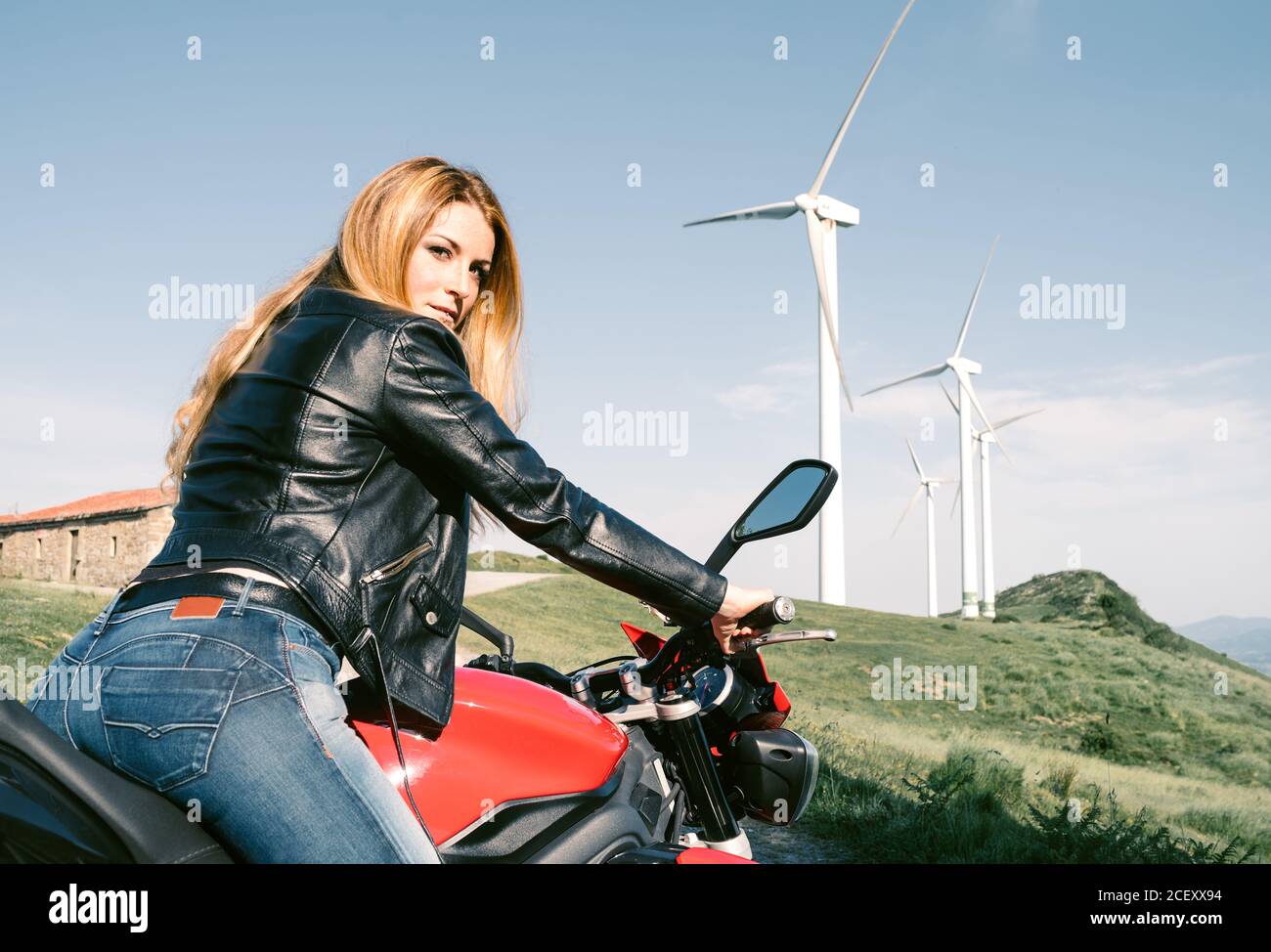 Vue latérale de bas angle d'une motard femme brutale assise sur moto sur  une route sablonneuse en été et regardant la caméra Photo Stock - Alamy