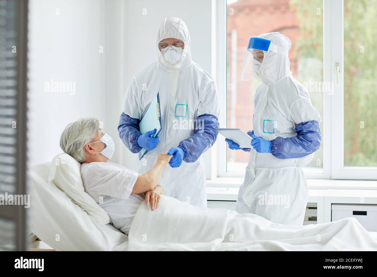 Médecins méconnaissables portant des combinaisons de protection avec des gants, des masques et des lunettes travaillant avec le patient dans le service des maladies infectieuses Banque D'Images