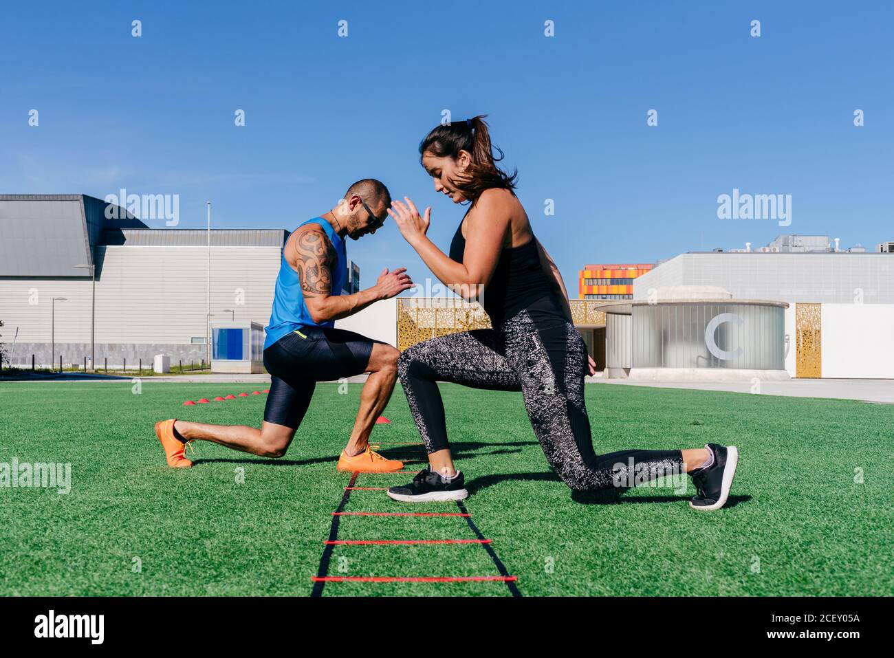 Vue latérale du corps de l'homme et de la femme sportifs qui font des fentes tout en s'exerçant avec l'échelle d'agilité sur une pelouse verte herbeuse sur un terrain de sport Banque D'Images