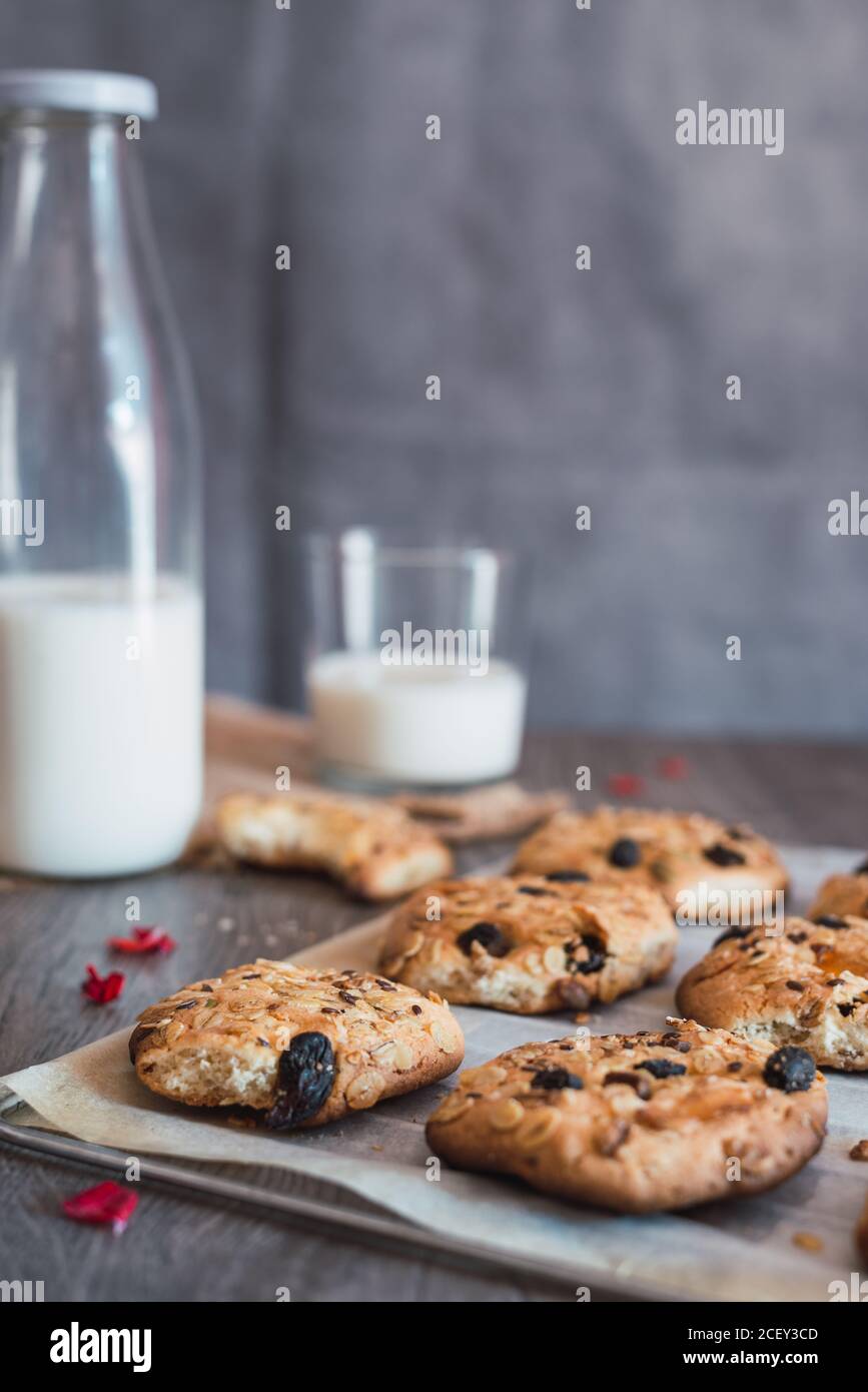 Délicieux biscuits de flocons d'avoine fraîchement cuits sur du papier de cuisson placé sur la table près de la bouteille et du verre avec du lait pendant le petit déjeuner Banque D'Images