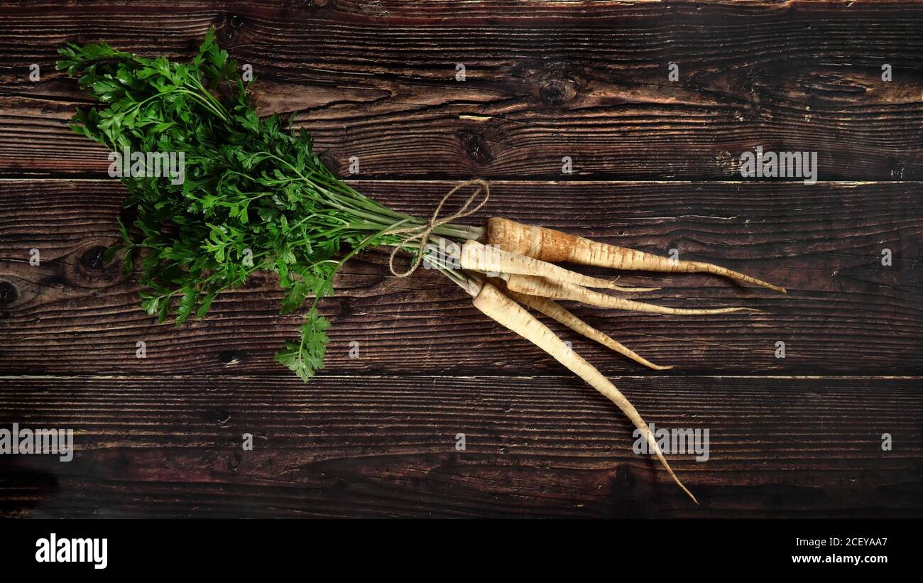 Bouquet de racines de panais avec des feuilles vertes sur un panneau rustique en bois sombre, vue d'en haut Banque D'Images