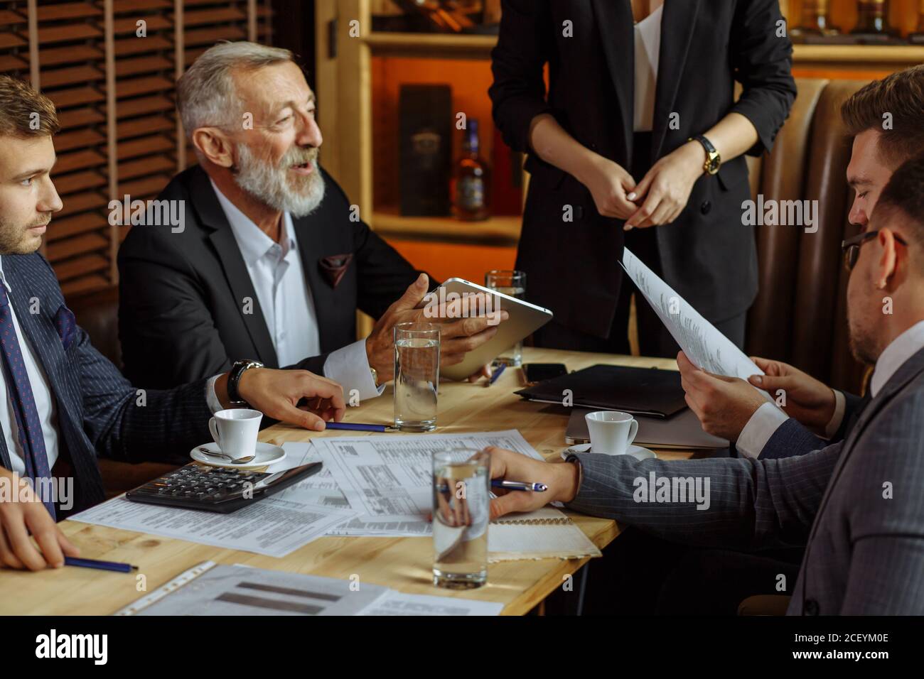 les hommes d'affaires en costume élégant s'assoient à table dans un bureau confortable discuter des plans stratégiques pour la diffusion future de différents documents dans devant Banque D'Images