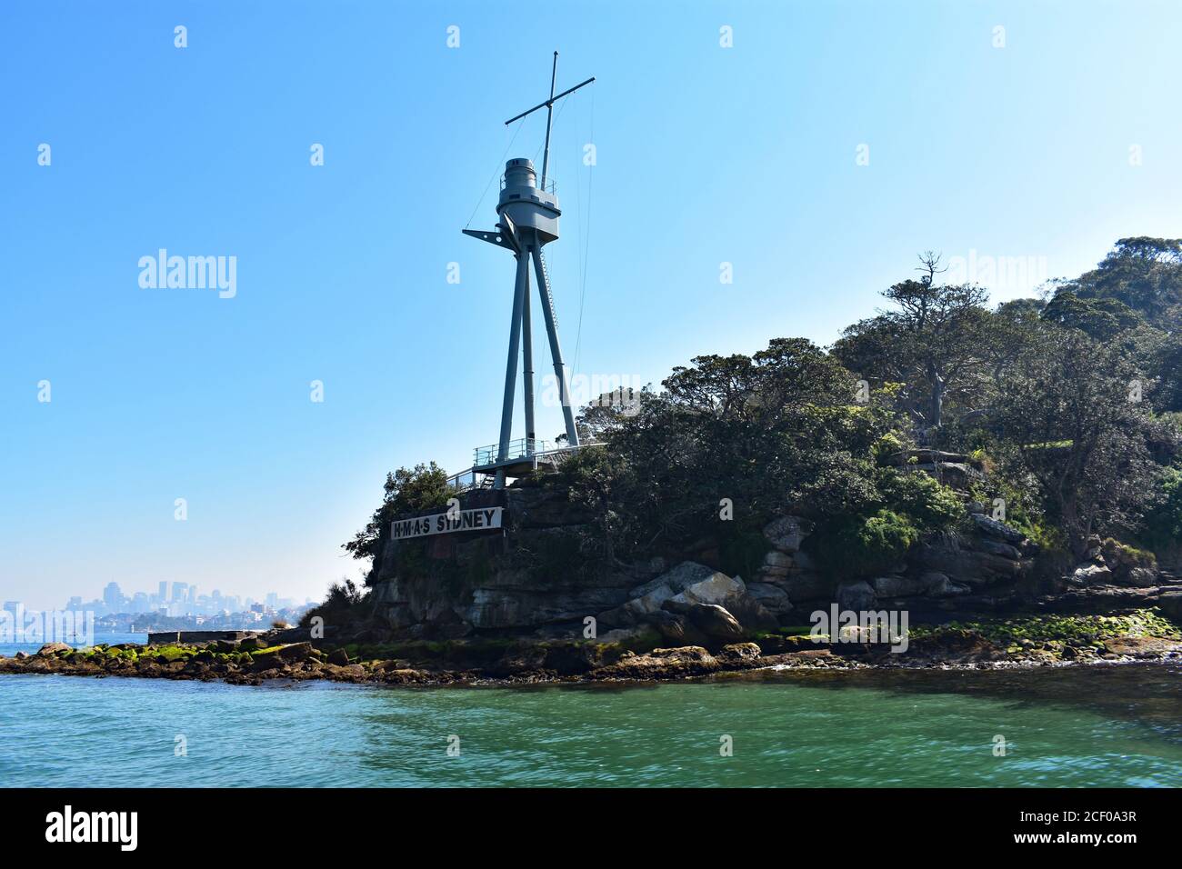 H.M.A.S Sydney Memorial Mast on Bradleys Head dans le port de Sydney par temps clair. Le quartier des affaires de Sydney est visible de l'autre côté du port dans la brume lointaine. Banque D'Images