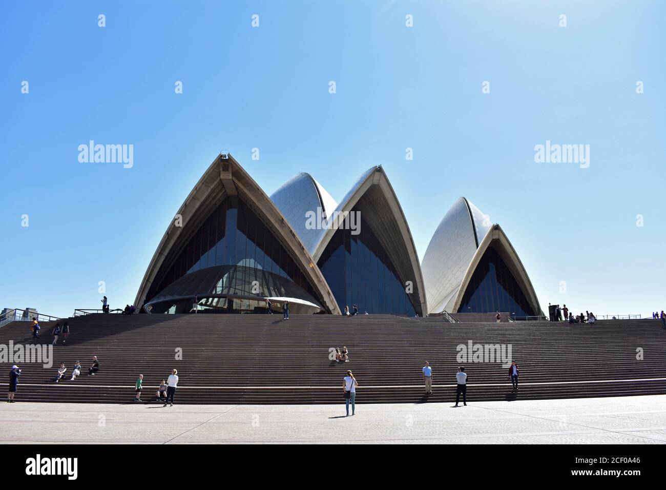 Visiteurs et touristes dans les escaliers menant à l'Opéra de Sydney. La ligne de toit dentelée est contre un ciel bleu Uni. Nouvelle-Galles du Sud, Australie Banque D'Images