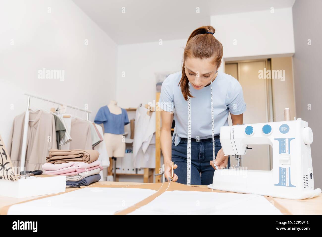 Lieu de travail de couturière tailleur. La jeune femme designer découpe le  motif de tissu de la ligne d'esquisse avec des ciseaux pour la confection  de robes et de vêtements Photo Stock -