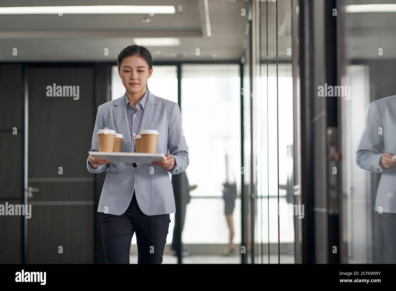 jeune stagiaire asiatique portant un plateau de tasses de café dans le bureau de l'entreprise Banque D'Images