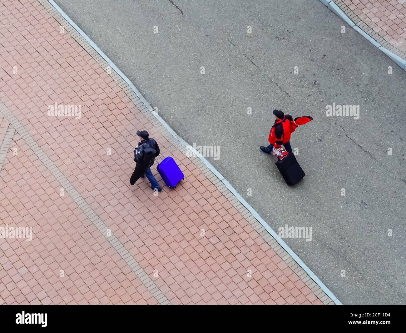 Des hommes avec des valises sur roues marchent le long de la route dans la rue. Vue de dessus Banque D'Images