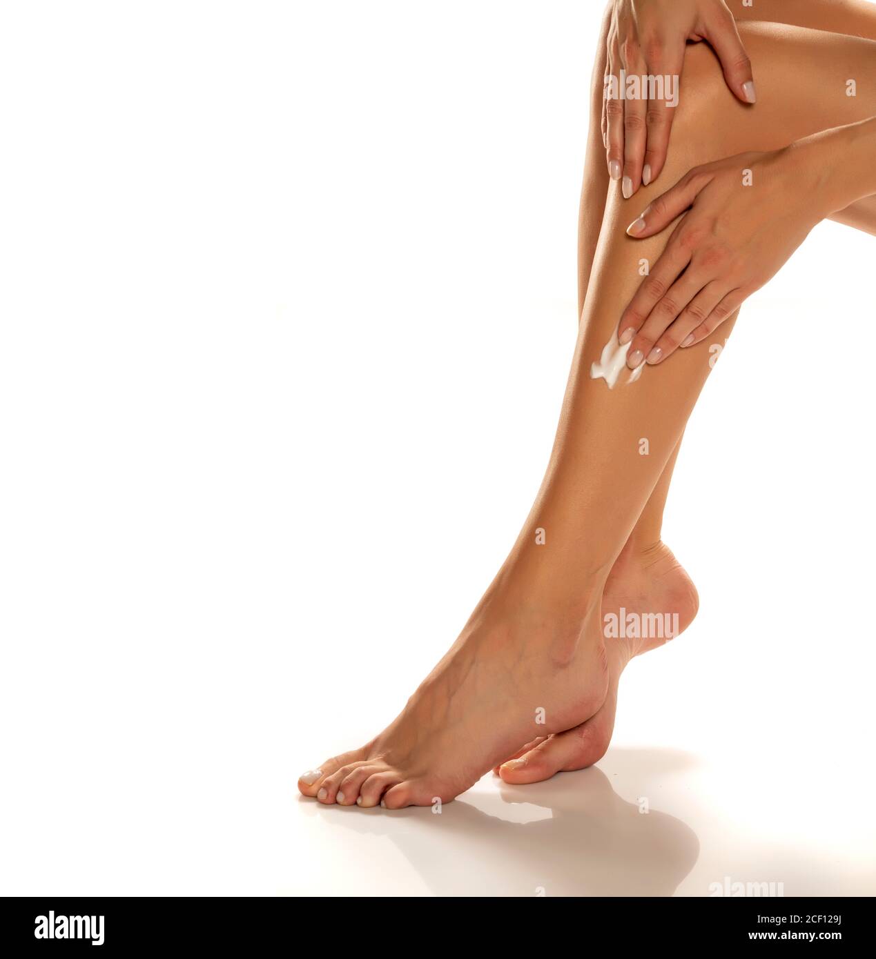 femme appliquant de la lotion sur ses jambes sur fond blanc Banque D'Images