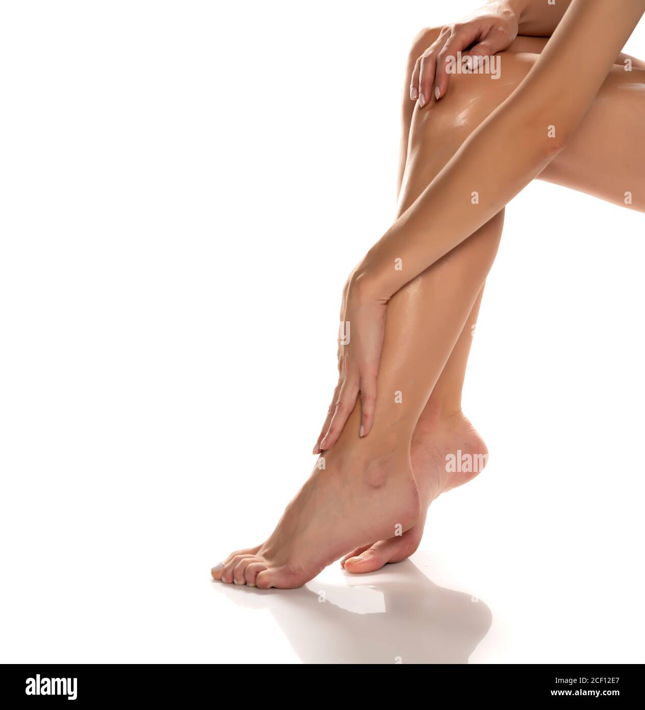 femme appliquant de la lotion sur ses jambes sur fond blanc Banque D'Images