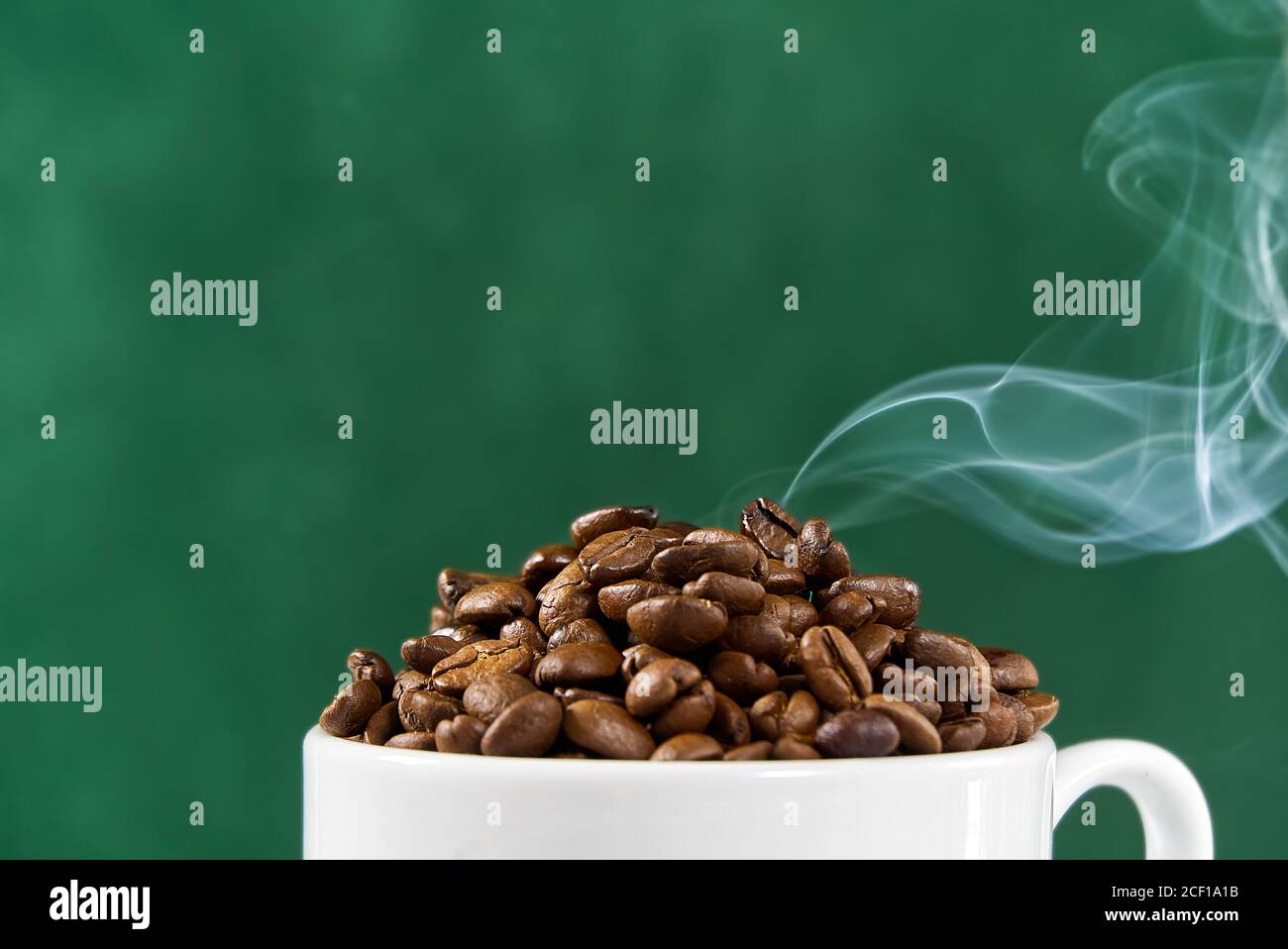 Concept de la journée internationale du café. Tasse de café blanc en gros plan pleine de grains de café sur fond vert avec fumée sur le dessus. Banque D'Images