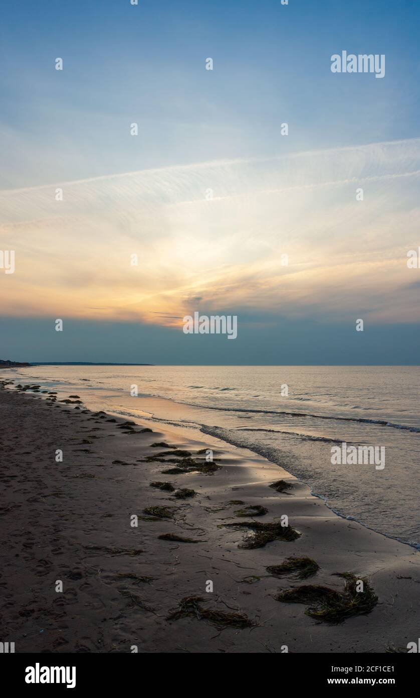 Plage déserte au crépuscule. Le coucher du soleil se reflète sur les eaux calmes de l'océan. Cavendish Beach, parc national de l'Île-du-Prince-Édouard, Canada Banque D'Images