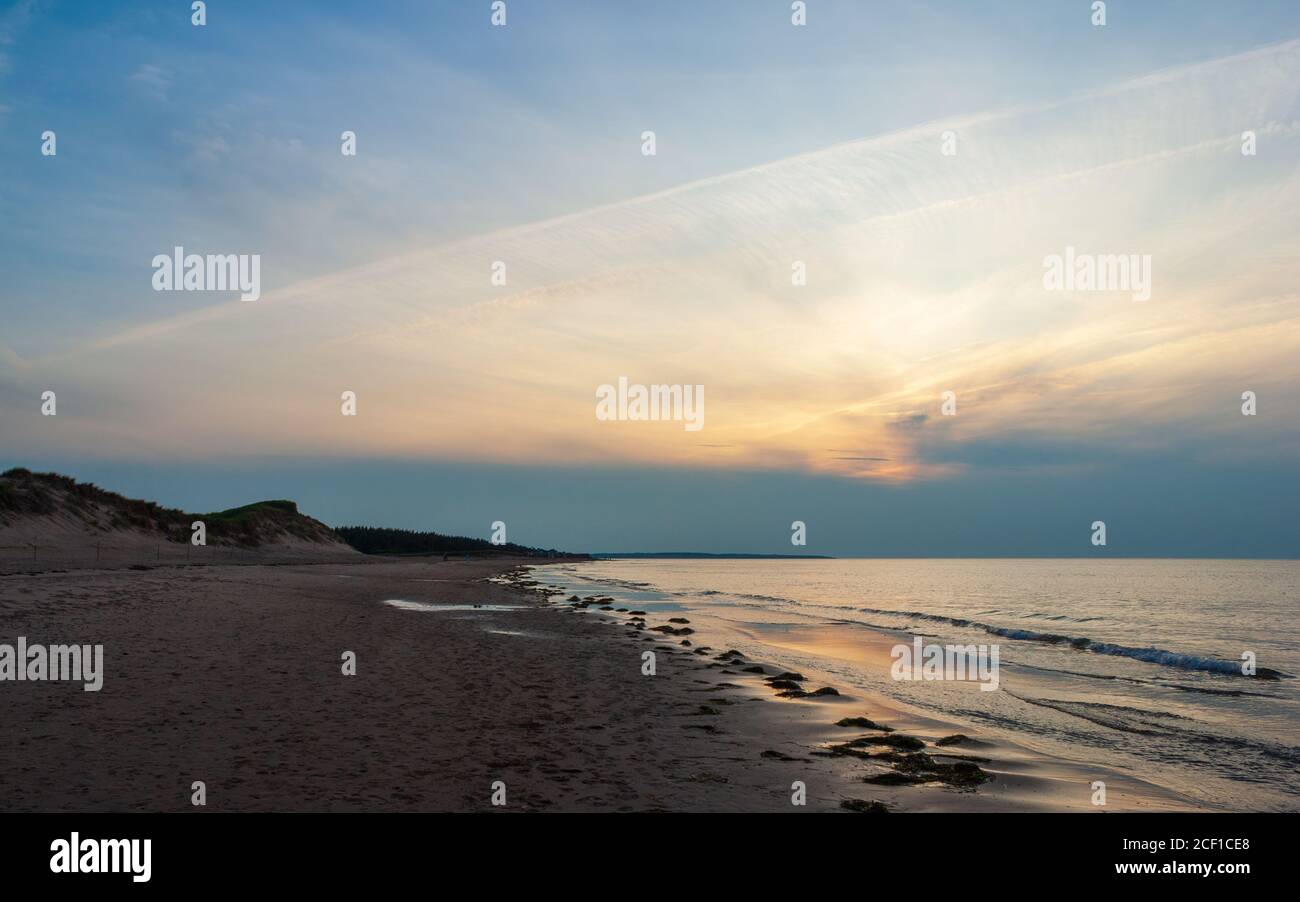 Plage déserte au crépuscule. Le coucher du soleil se reflète sur les eaux calmes de l'océan. Cavendish Beach, parc national de l'Île-du-Prince-Édouard, Canada Banque D'Images