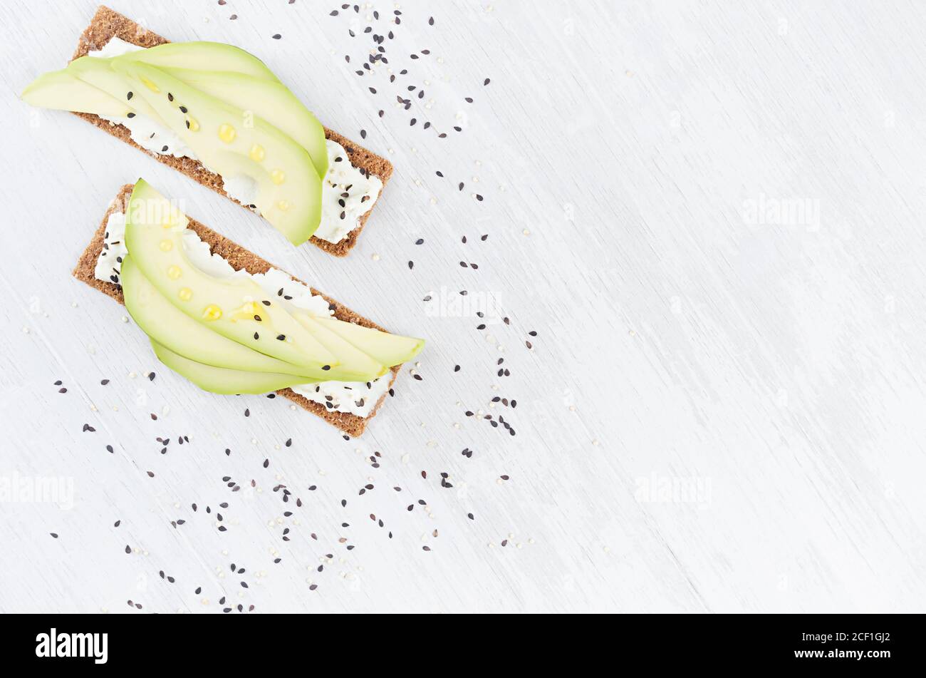 Petit déjeuner diététique sain de croustilles pain grillé plat de seigle avec tranches d'avocat frais, huile d'olive, graines de sésame noir, fromage à la crème sur fond de bois blanc, à Banque D'Images