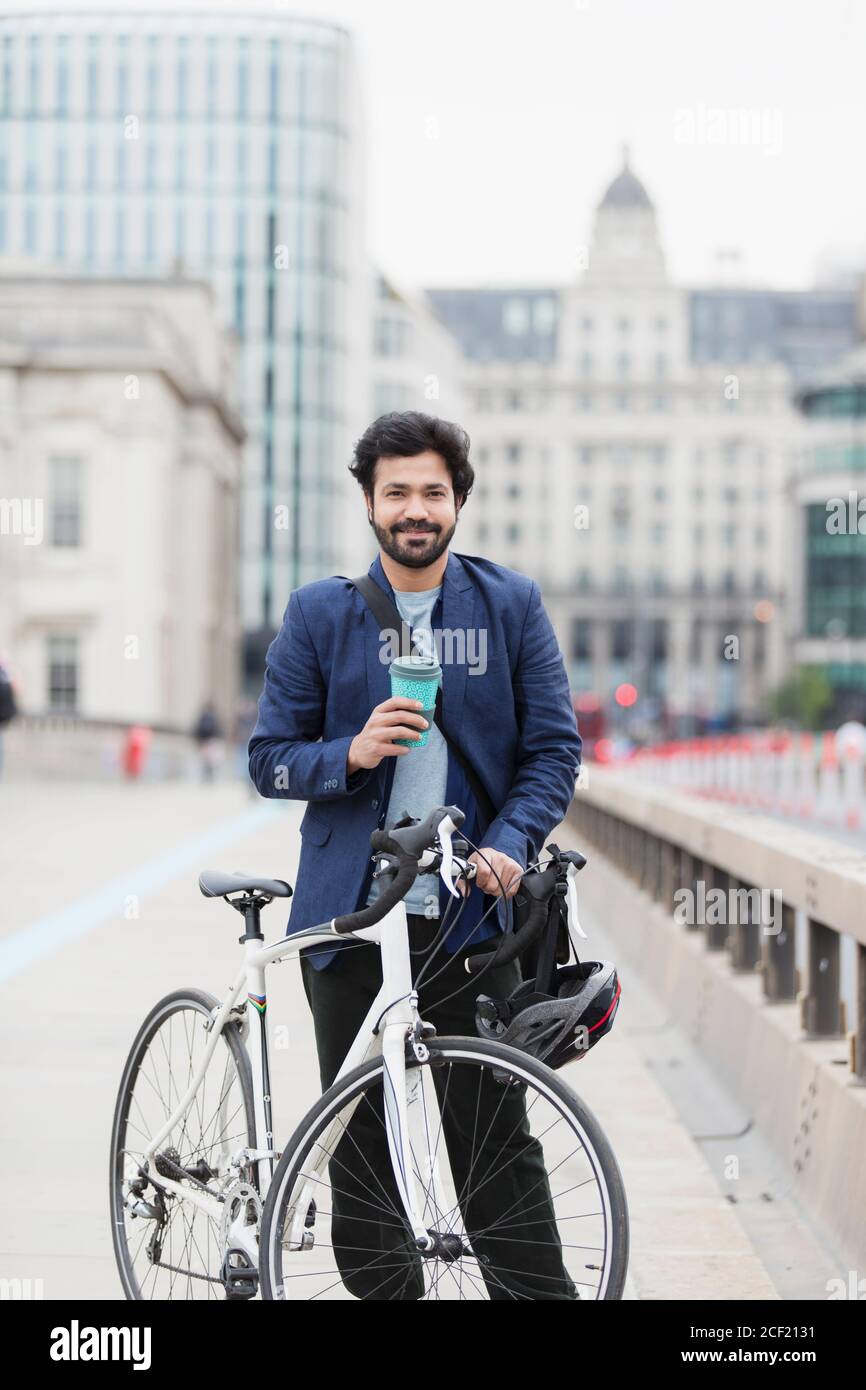 Portrait d'homme d'affaires souriant avec café et vélo sur le pont de la ville Banque D'Images