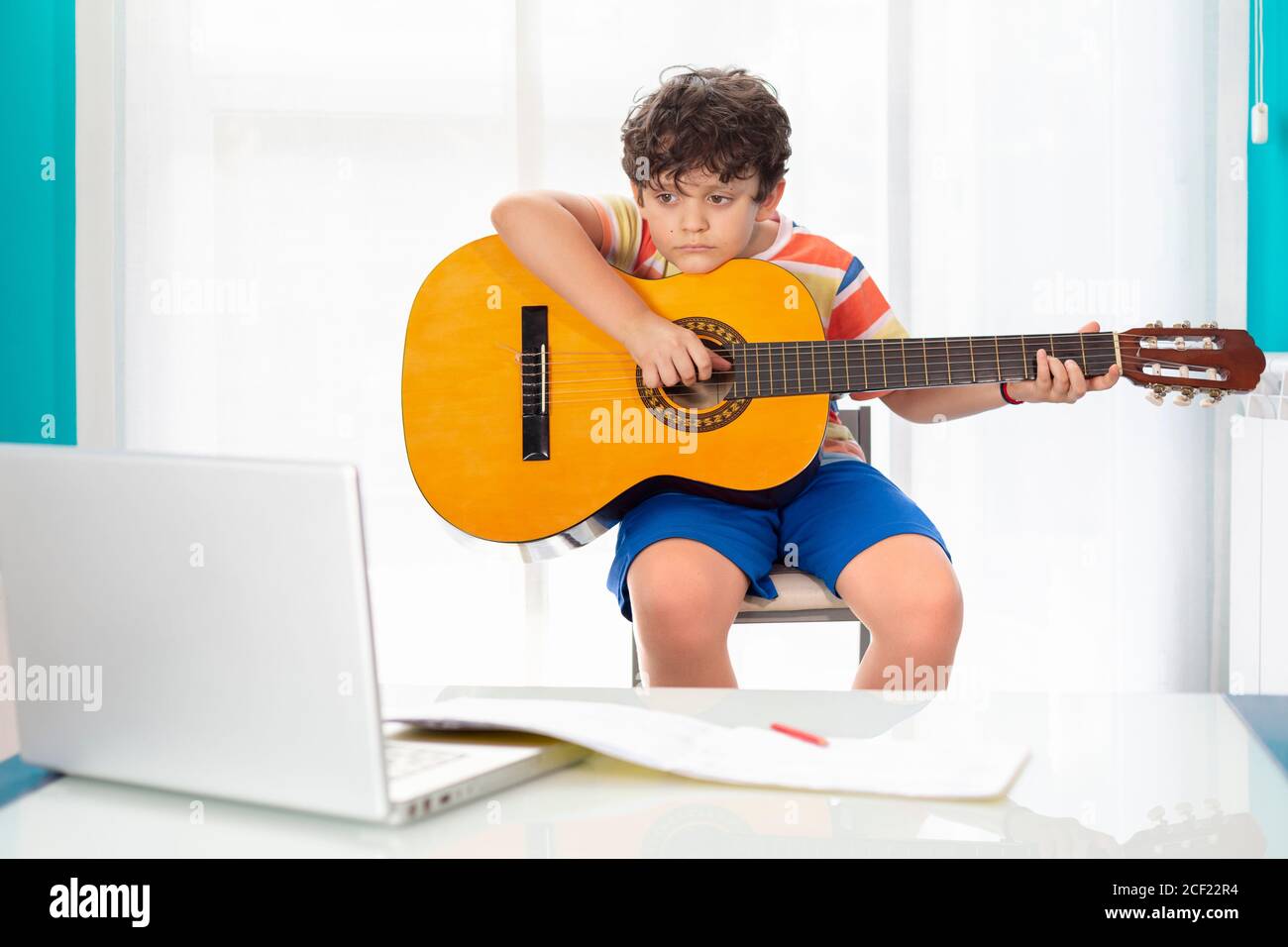 Petit garçon à la maison jouant de la guitare espagnole devant son ordinateur portable. Concept de classe de guitare en ligne. Banque D'Images