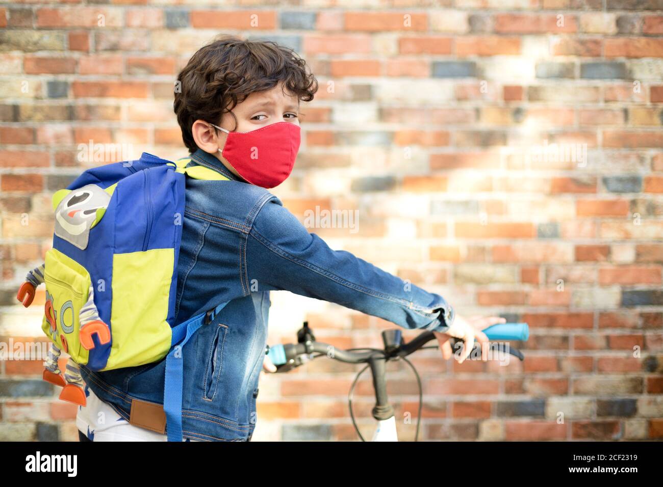 Petit garçon avec un masque facial et un sac à dos à vélo à l'école après la quarantaine Covid-19. Banque D'Images