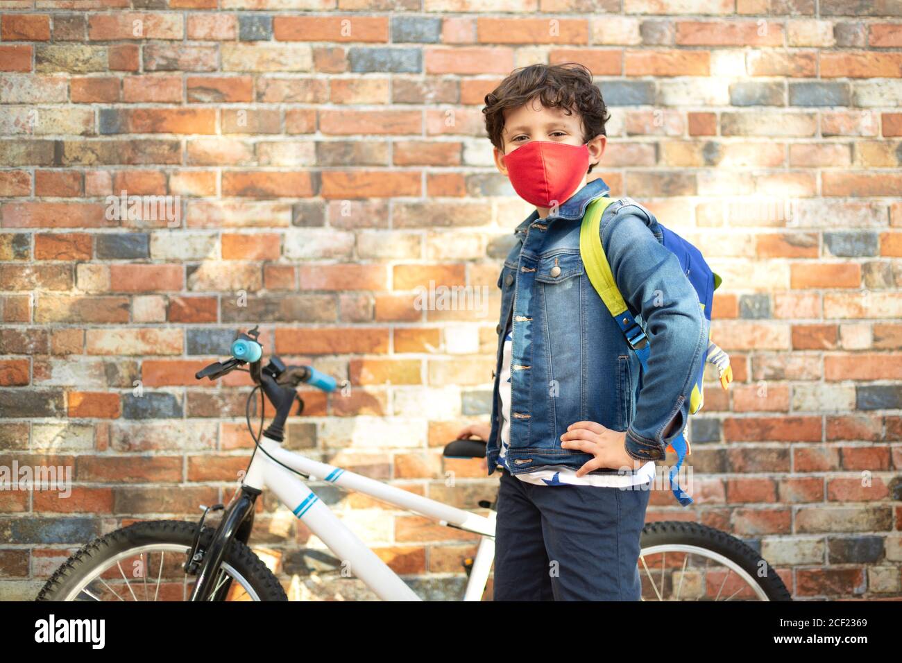 Petit garçon avec son vélo prêt à aller à l'école. Il est dans la rue et porte un masque. Banque D'Images