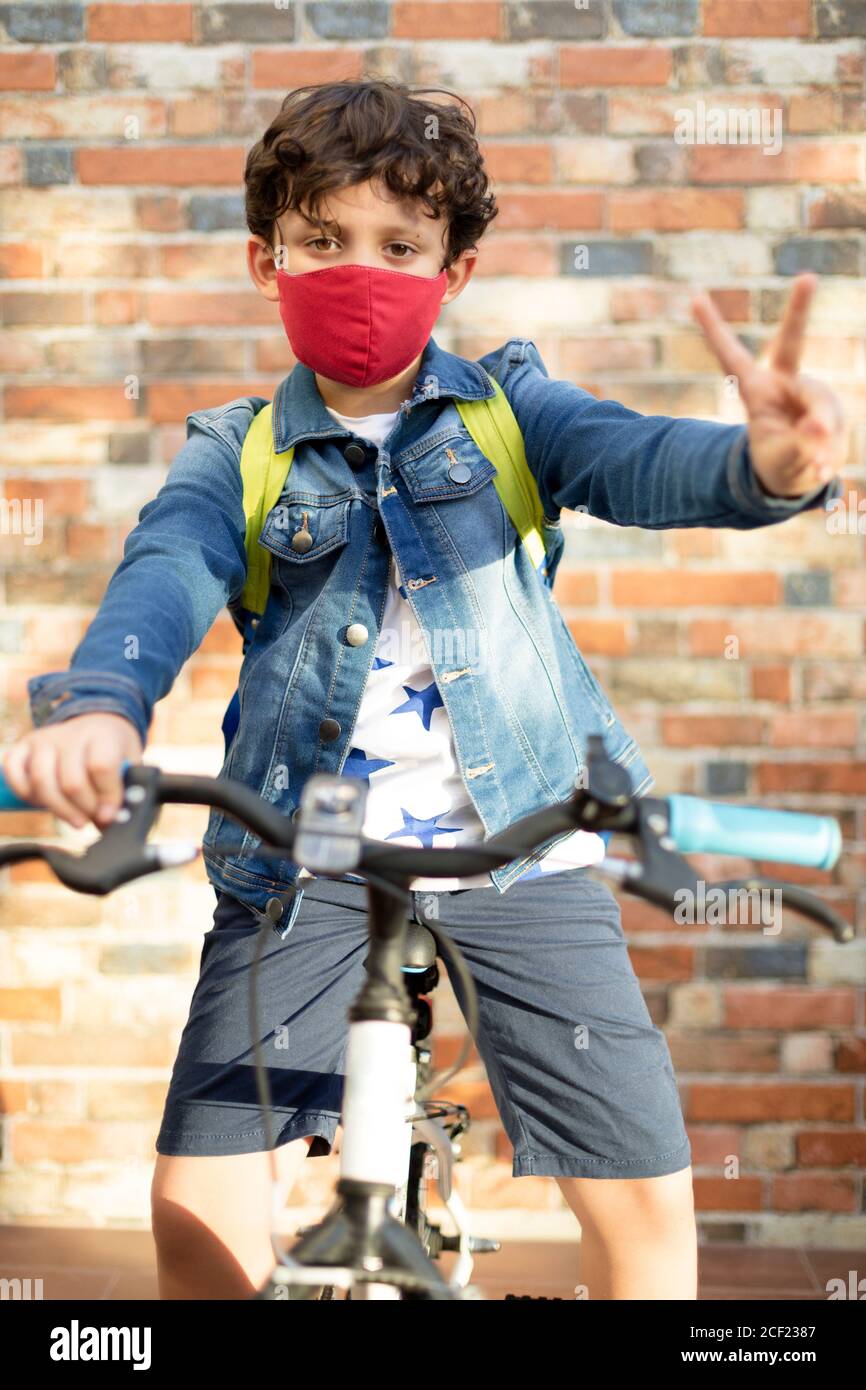 Un petit garçon sur un vélo. Il est dans la rue et porte un masque pour prévenir la pandémie Covid-19. Concept de retour à l'école et nouveau Banque D'Images