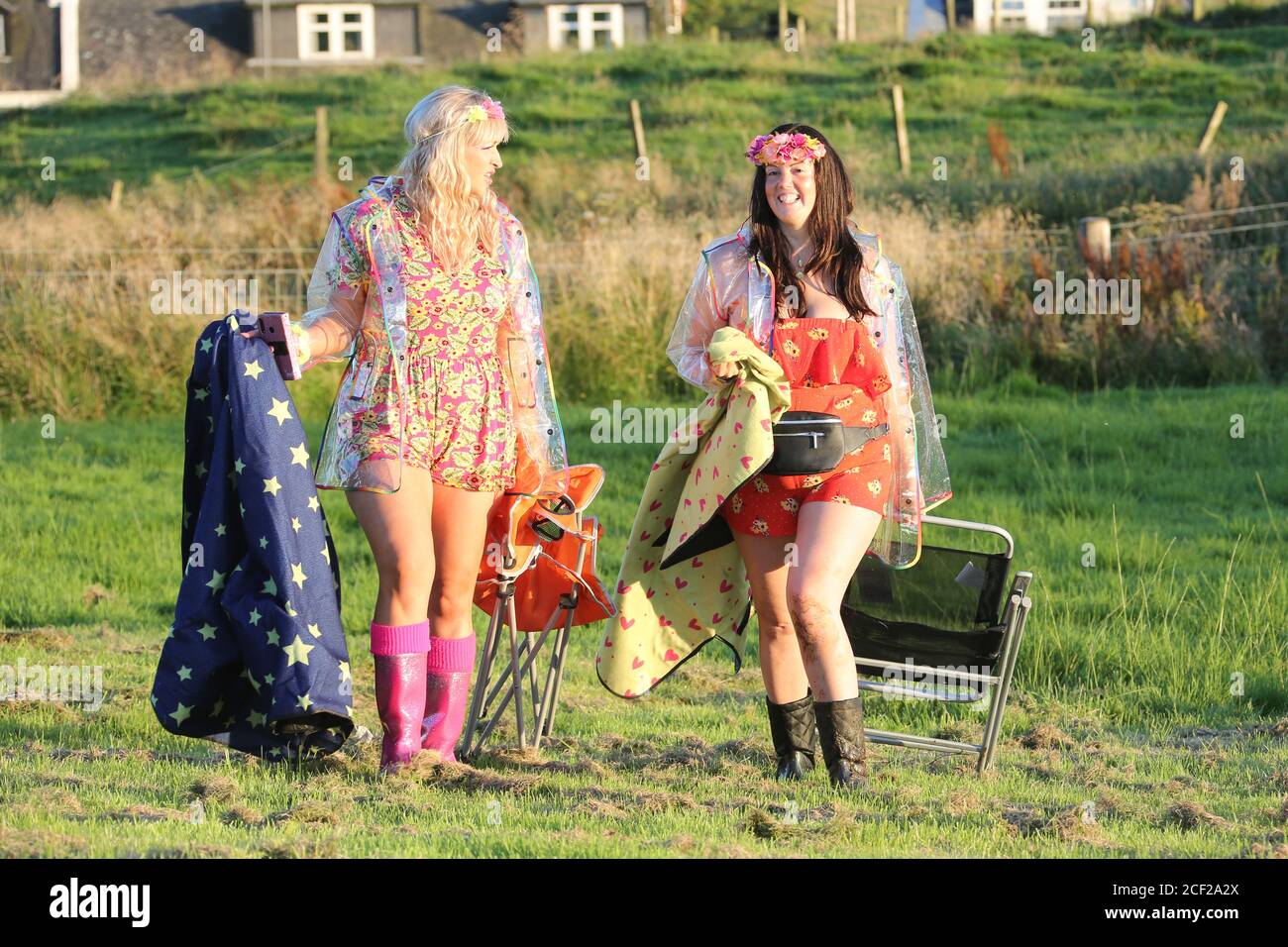 Fenwick, Ayrshire, Écosse, 24 août 2020 : les amis Claire Stewart et Leona Young ne pouvaient pas faire Glastonbury cette année en raison de la pandémie de coronavirus, donc décidé d'avoir leur sur le mini-festival .Avec des fleurs dans leurs cheveux, se sourit, voir à travers des manteaux en plastique en cas de pluie les filles dansaient à la musique sur leurs téléphones.Festival vêtements de pluie et Mac en plastique avec le modèle de puits coloré libéré Banque D'Images