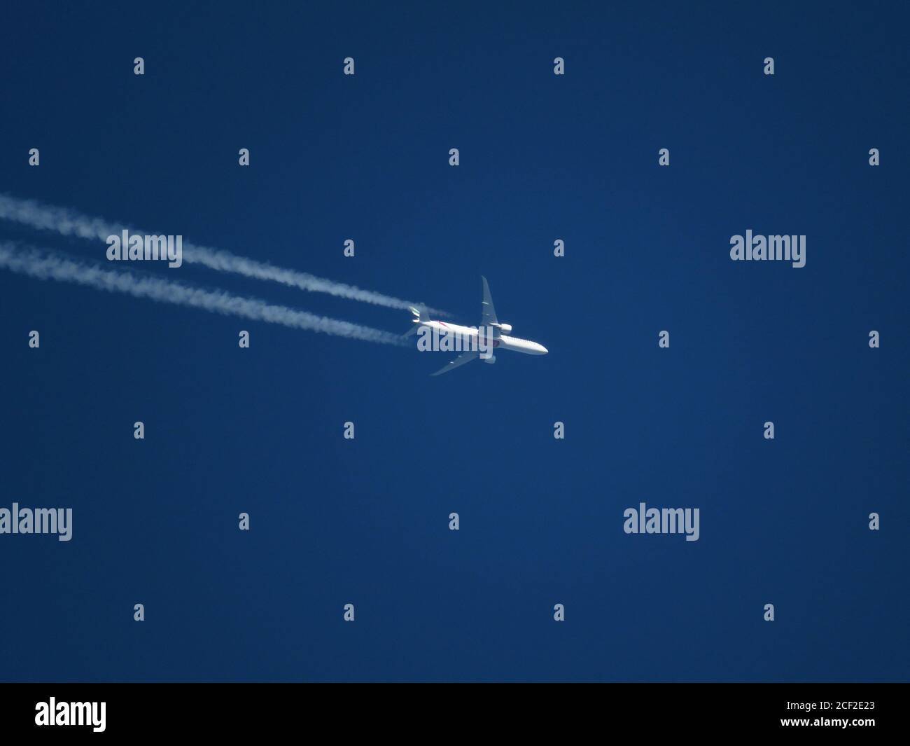 Téléplan de l'avion de ligne à double moteur Emirates volant à haute altitude dans un ciel bleu clair avec des contrailles Banque D'Images