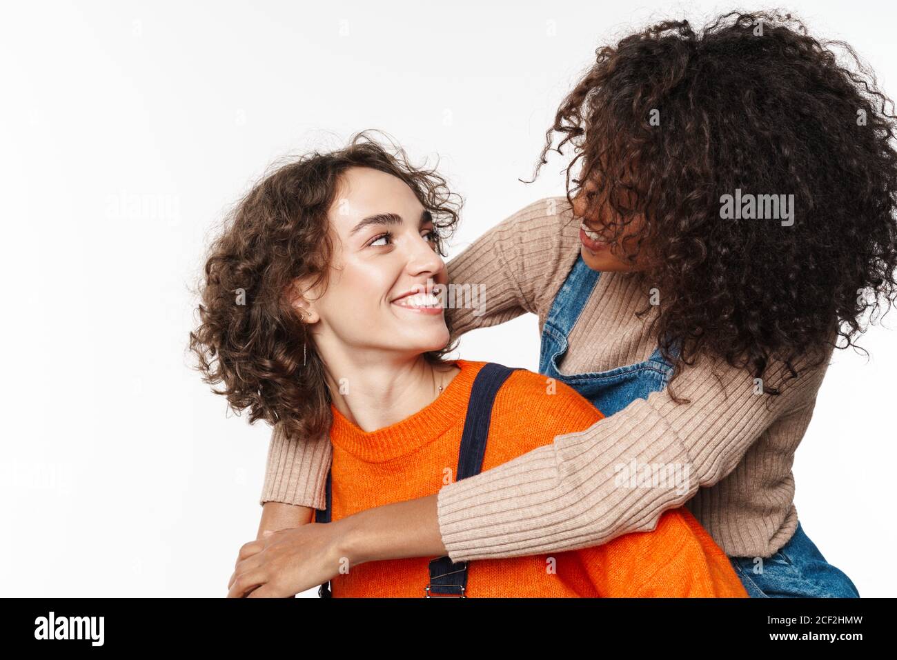 Image de l'incroyable optimiste heureux multiracial filles amis en denim combinaisons isolées sur fond de mur blanc ayant le plaisir. Banque D'Images